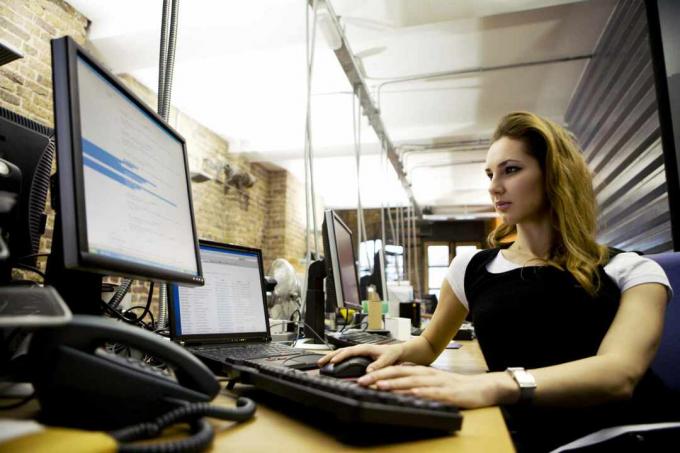 Une femme assise à un bureau utilisant un ordinateur portable avec un clavier et un moniteur externes.