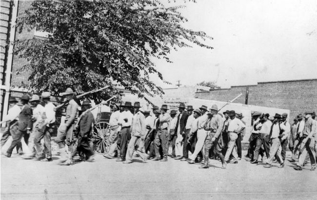 Un groupe de soldats de la Garde nationale, portant des fusils avec des baïonnettes attachées, escorte des hommes noirs non armés vers un centre de détention après le massacre de Tulsa Race, Tulsa, Oklahoma, juin 1921.
