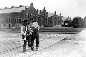 Deux militaires se tiennent à côté du Pullman Building et des voitures de train avec les bras verrouillés et une bouteille d'alcool pendant la grève du Pullman de Chicago en 1894