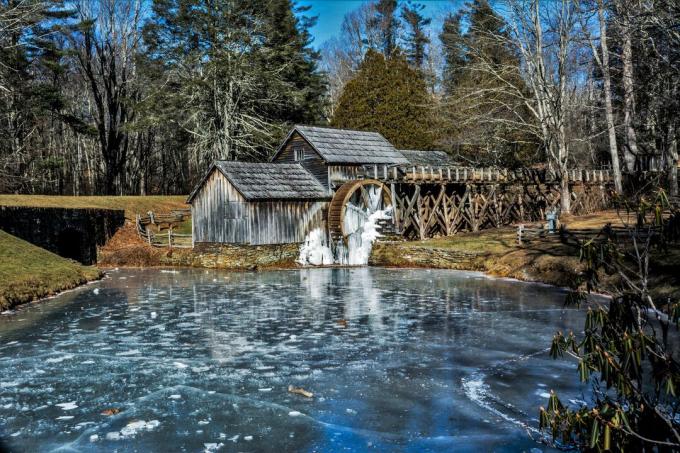 Moulin à roue à eau construit sur une rivière entourée d'arbres.