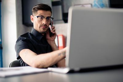 Homme à lunettes au téléphone à l'aide d'un ordinateur portable