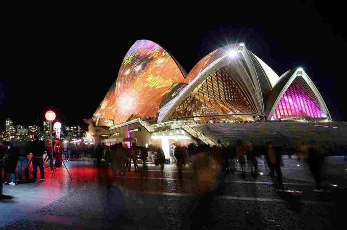 Vue de nuit d'un bâtiment en forme de coquille éclairé de couleurs vives près d'un plan d'eau