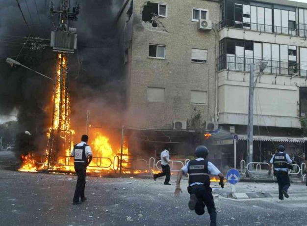 Des policiers israéliens se précipitent sur les lieux d'un pylône électrique en feu et d'un bâtiment endommagé quelques instants après qu'une volée de roquettes du Hezbollah a frappé le 13 juillet 2006 dans la ville nord de Nahariya, en Israël.