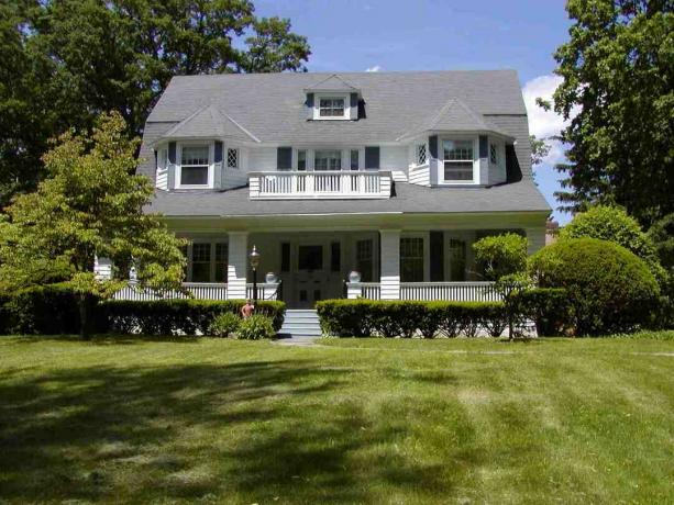 Grande maison blanche avec un énorme toit gris à l'avant et une grande pelouse verte