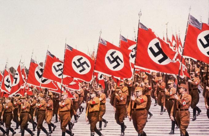 Nazis marchant en formation avec des drapeaux lors d'un rassemblement.