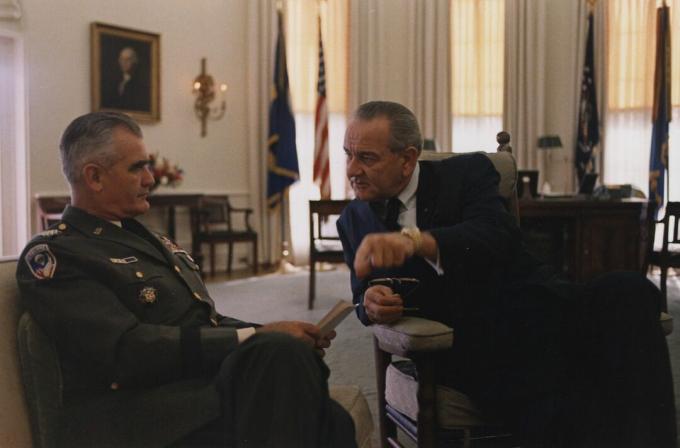 Le général William Westmoreland, en uniforme de l'armée américaine et assis s'entretient avec le président Lyndon B. Johnson dans le bureau ovale.