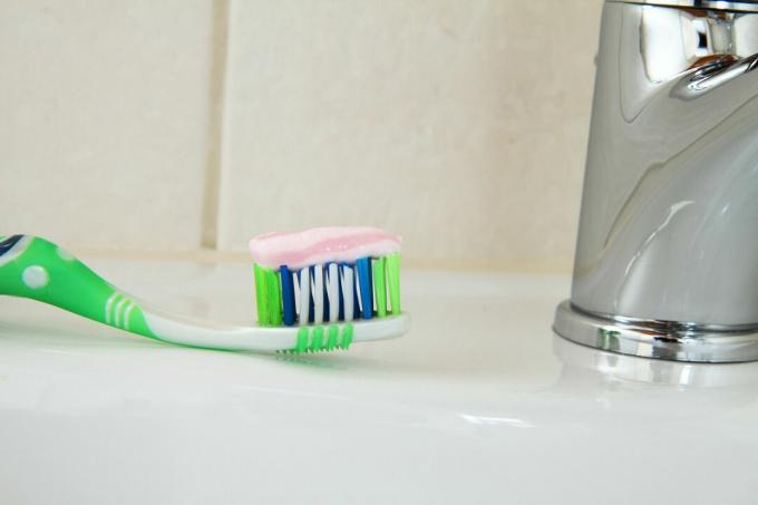 Gros plan d'une brosse à dents avec du dentifrice dessus assis sur l'évier.