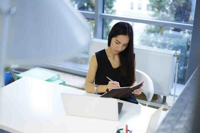 Femme d'affaires écrivant dans un cahier devant l'ordinateur