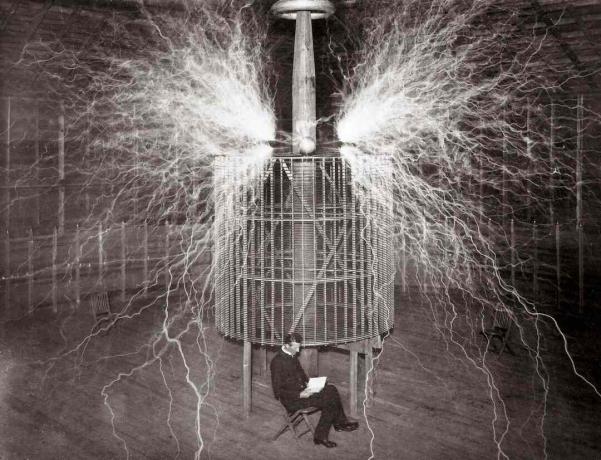 Nikola Tesla assis dans son laboratoire de Colorado Springs à côté de son énorme 