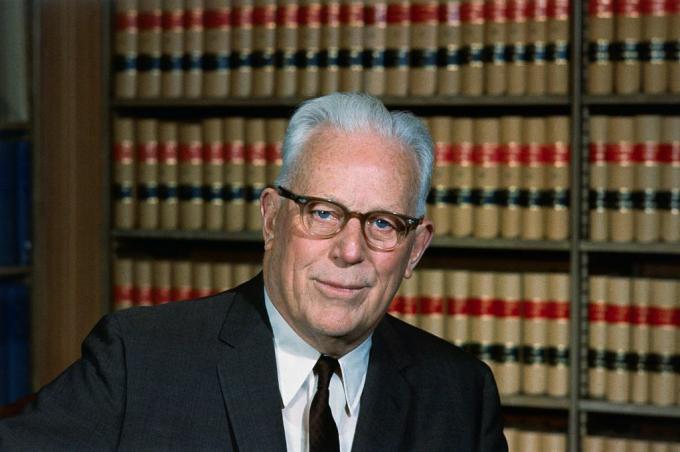 Photographie couleur de l'ancien juge en chef de la Cour suprême des États-Unis, Earl Warren, assis dans sa bibliothèque juridique.