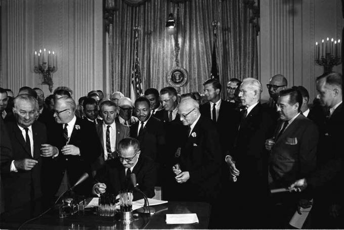 Le président Lyndon B. Johnson signe le Civil Rights Act de 1964 sous le regard de Martin Luther King, Jr.et d'autres.