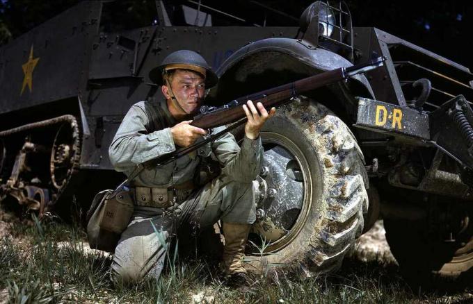 Un soldat américain s'agenouille avec un M1 Garand devant un half-track.